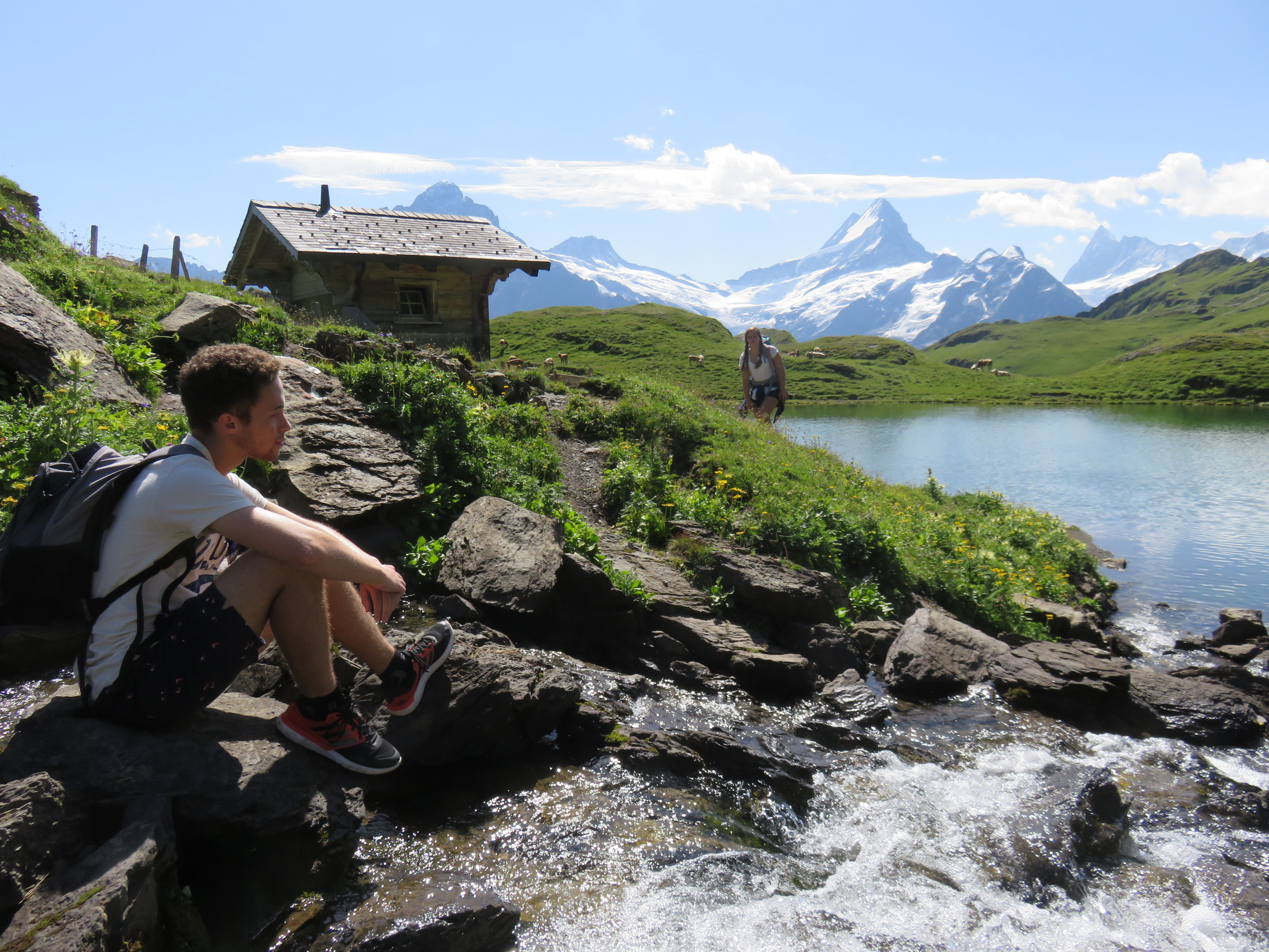 Matthew sitting next to a lake, with the mountains in the background in Switzerland.
